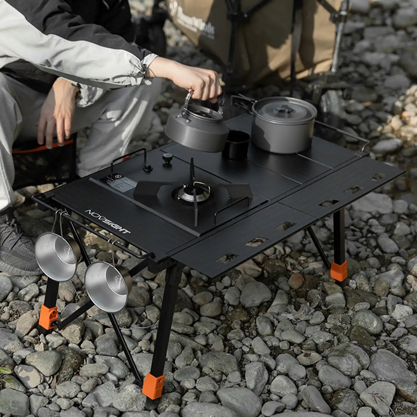 Portable camping stove with pots and pans on a rocky ground