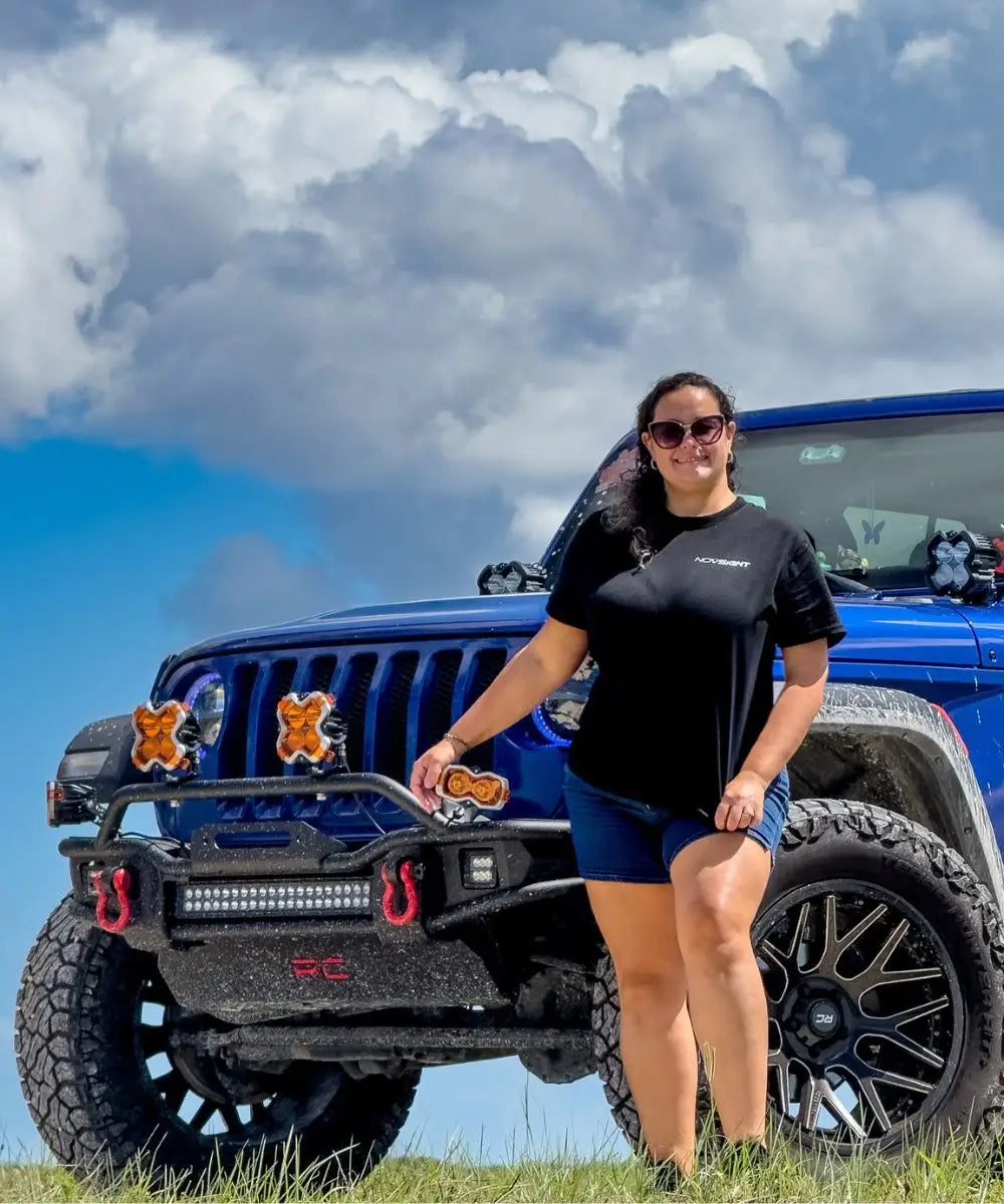 Person standing next to a blue Jeep with a clear sky background