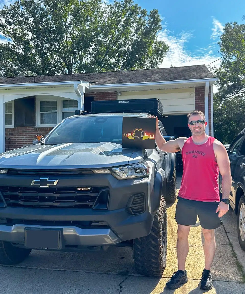 Man holding a halo pod light's laptop with a colorful design in front of a Chevrolet truck