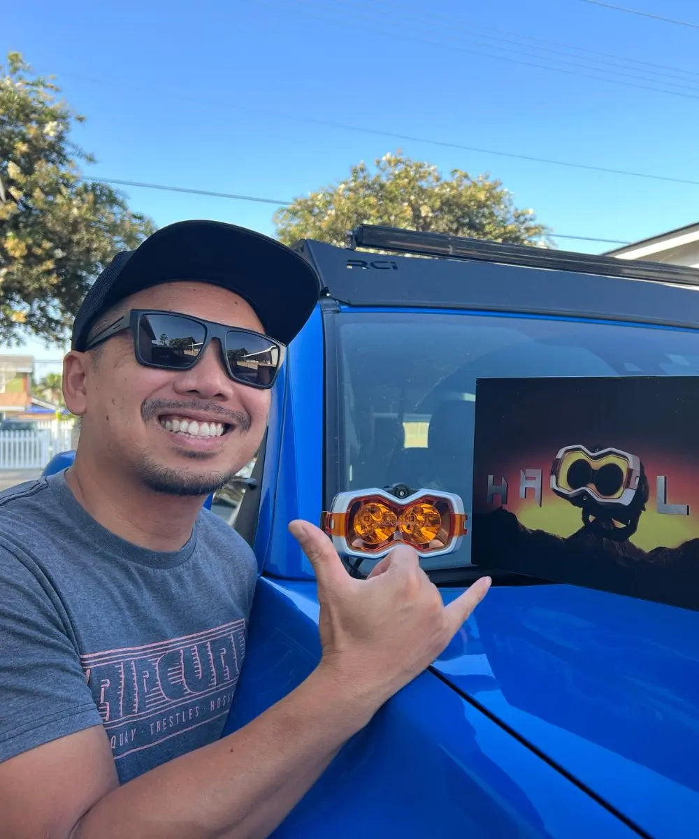 Man pointing at a blue vehicle with a screen displaying graphics, outdoors.