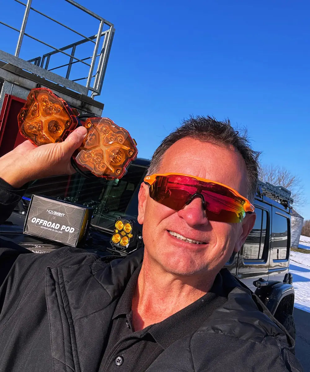 Person holding novsight X series off-road lights with a vehicle and clear blue sky in the background