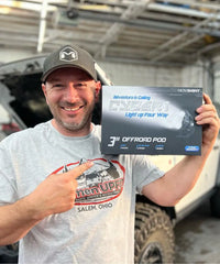 Man holding a box of Novolight off-road pod in front of a vehicle